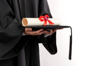 Pessoa vestida com beca segura diploma e capelo (chapéu da formatura)