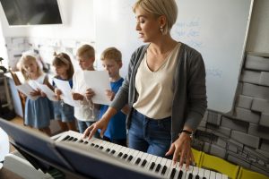 Professora tocando piano enquanto orienta crianças em uma aula de música.