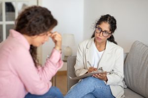 Mulher angustiada em consulta com terapeuta, que segura uma prancheta e faz anotações, em um ambiente acolhedor.