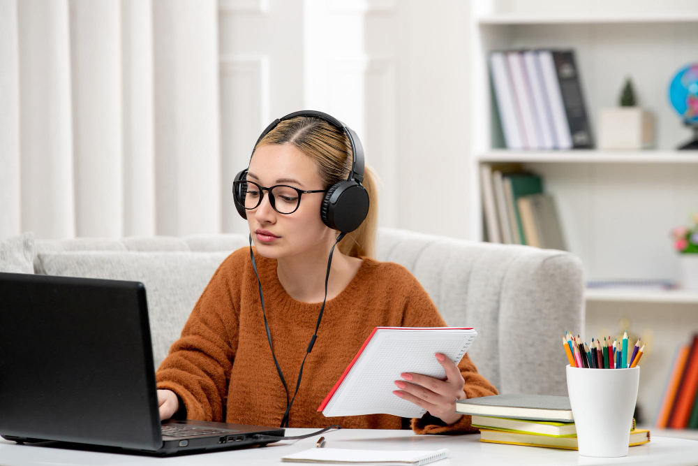 Jovem estudando em casa com fones de ouvido, laptop e caderno.