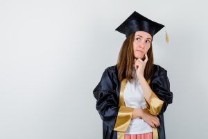 Mulher vestindo beca de formatura com expressão pensativa.
